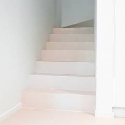 Strakke witte trap met beton ciré afwerking in een minimalistisch interieur.