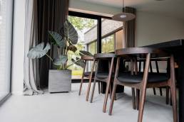 Moderne eetkamer met houten stoelen en grote plant, op een strakke beton ciré gietvloer.